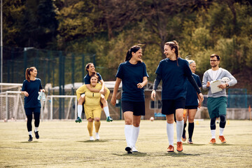 Obraz na płótnie Canvas Cheerful female players talk after soccer practice at stadium.