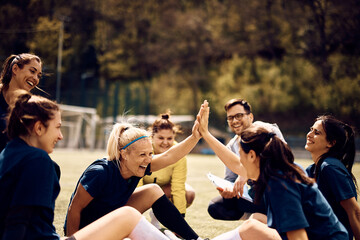 Happy soccer players giving high five and having fun on playing field.