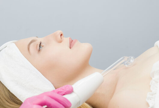 A beautiful young woman receiving a darsonval electric massage procedure in a beauty salon. Hardware cosmetology. Selective focus.