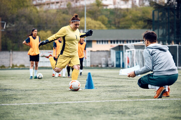 Female goalie shooting ball during soccer training at stadium.