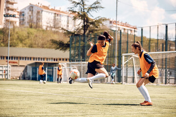 Skillful sportswoman jumping while practicing with ball on soccer training. © Drazen