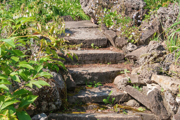 Old stone staircase made of gray large rough stones with green grass