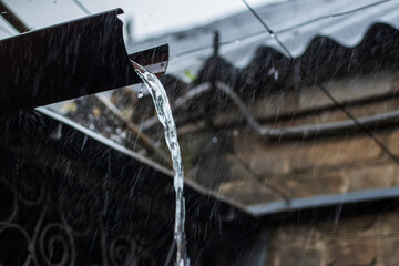 Rain water is pouring from the green draining gutter on the pavement, selective focus.