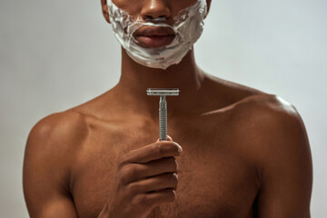 Focus of razor in hand of guy with foam on face