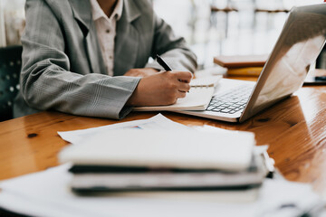 woman writing making list taking notes in notepad working on laptop indoors
