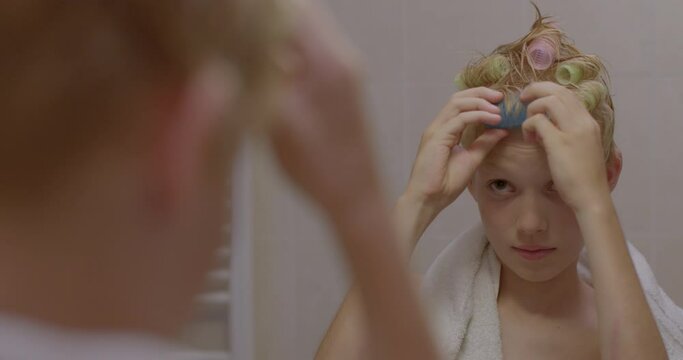 A boy uses curlers on his hair in front of a mirror. Examines his reflection, poses. Mental condition people have an inflated sense of their own importance, deep need for attention and admiration.
