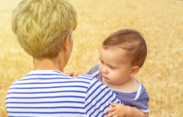 baby boy,toddler,infant in wheat field with grandmother.sunny rays from corner summer day,harvest food concept.golden wheat ears.granny holding in arms adorable kid.bread making,whole grains.