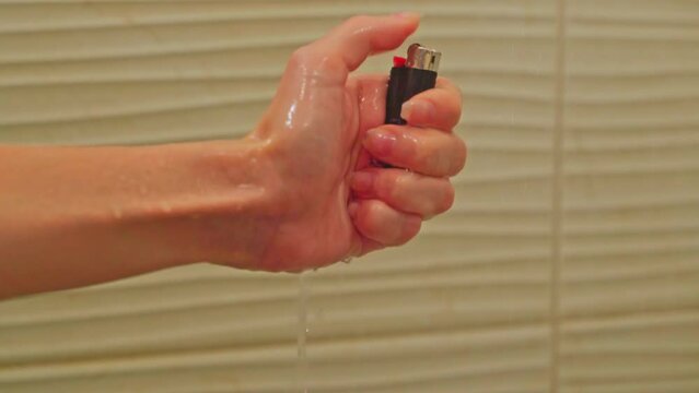 A close-up of a woman's hand tries to light a lighter in the shower under water but she fails. Bad habits. Trying to light a cigarette in the shower.
