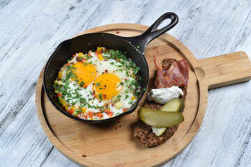 Fried eggs in a pan with vegetable tartare, bacon, pickled cucumber and cream cheese. Breakfast