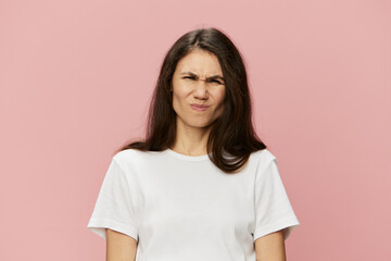 Fototapeta premium a funny, funny, sweet woman with dark hair color stands in a white t-shirt on a pink background and closes her face tightly with her eyes closed. Horizontal photo with blank space for advertising text