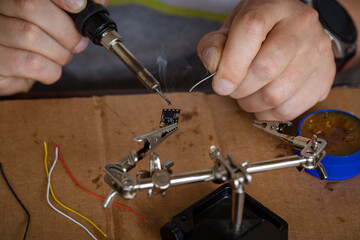 The hand holding the tin, a soldering iron solder the chip in place. a man solders a wire to a microcircuit