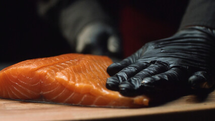 Close-up chef with piece of red salmon. Professional chef in black gloves holds piece of fresh salmon and is ready to cut it