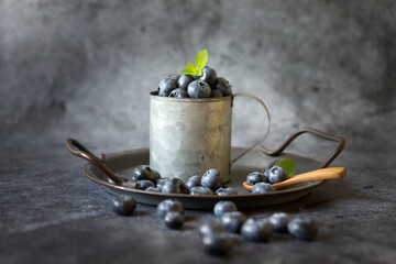 Ripe blueberries in an iron cup on different surfaces.