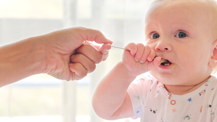 Mother is Feeding a baby from a spoon. Mom feeds a 9 month baby with fruit puree from a spoon, close-up, high key. Infant boy eats sitting on baby's chair. Mother cares about little son.