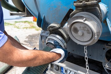 The man connects a 4 inch PVC suction hose to the flange fitting on the trucks tank.