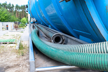 Long 4 inch PVC suction hoses lie next to the tank of the septic tank truck.