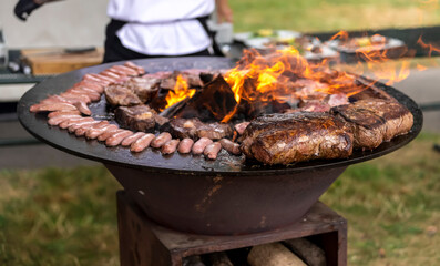 Grilling meat and sausages on a round barbecue with an open fire. Peknik