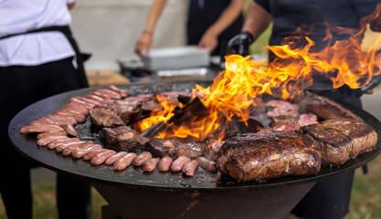 Grilling meat and sausages on a round barbecue with an open fire. Peknik