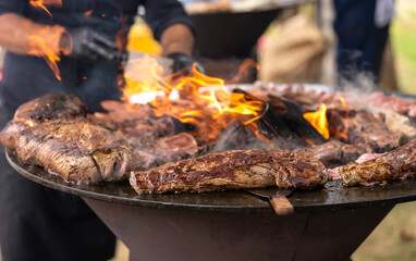 Grilling meat and sausages on a round barbecue with an open fire. Peknik