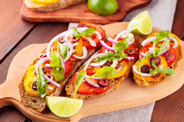 Healthy vegetarian tapas and lime on a cutting board. Vegetarian toasts with tomatoes, greens and olives. Open sandwiches on wooden boards. Top view
