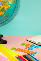 Back to school letters, with school supplies and a world ball on a pink table with a blue background.
