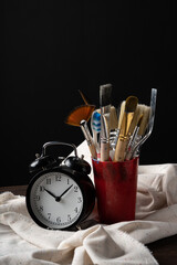 A glass with brushes and an alarm clock stand on a light rag on an oak board.