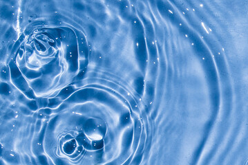 Naklejka na ściany i meble Flow of water is pouring on rippled water surface. Abstract background. Copy space for your design - stock photo