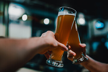 Two friends hands toasting with glasses of light beer at the pub or bar