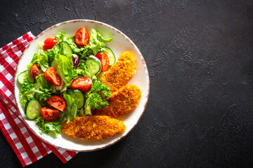 Chicken nuggets with fresh salad at dark stone table. Top view image with copy space.
