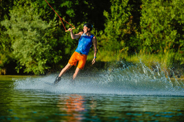 A professional wakeboarder rides on the lake in sunny weather, performing figures
