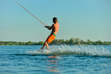 A professional wakeboarder rides on the lake in sunny weather, performing figures