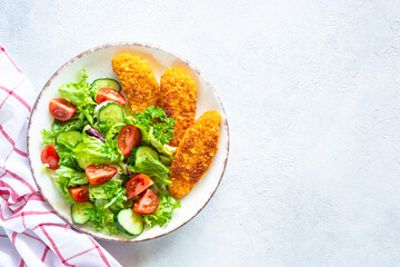 Chicken nuggets with fresh vegetable salad at white table. Top view image with copy space,
