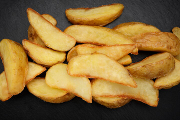 Fried potato wedges on black slate. Dark concrete
