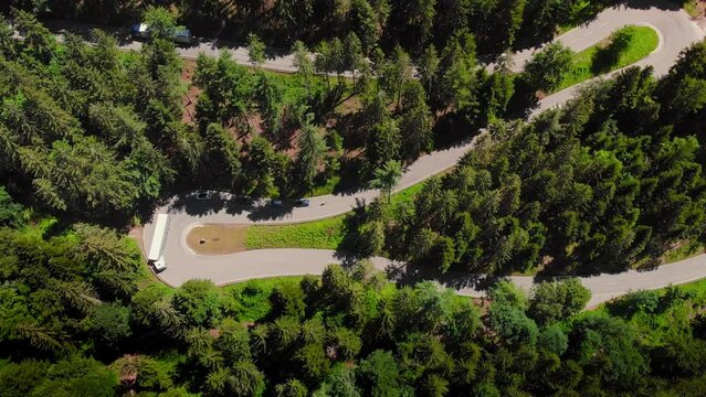 Footage of bendy mountain road from above, showing a truck and the traffic driving through the forest
