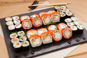 a large set of sushi rolls on a black stone plate
