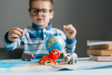 One toddler child studies the animal world with the help of a map and toy animals: lion, deer, Zebra, rhinoceros