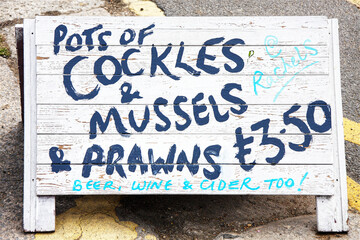 Sign advertising cockles mussels and prawns seafood at british seaside - obrazy, fototapety, plakaty
