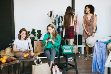 four young woman female caucasian and african students at swap party try on clothes, bags, shoes and accessories, change clothes with each other, second hand for things, zero waste life, eco-friendly