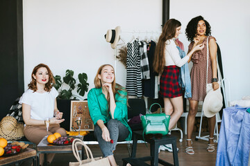 four young woman female caucasian and african students at swap party try on clothes, bags, shoes and accessories, change clothes with each other, second hand for things, zero waste life, eco-friendly