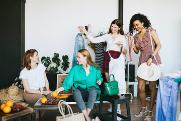 four young woman female caucasian and african students at swap party try on clothes, bags, shoes...