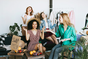 four young woman female caucasian and african students at swap party try on clothes, bags, shoes...