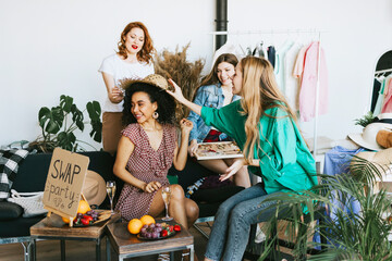 four young woman female caucasian and african students at swap party try on clothes, bags, shoes...