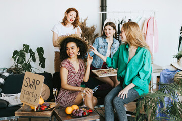 four young woman female caucasian and african students at swap party try on clothes, bags, shoes...