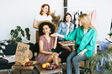four young woman female caucasian and african students at swap party try on clothes, bags, shoes...