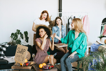 four young woman female caucasian and african students at swap party try on clothes, bags, shoes and accessories, change clothes with each other, second hand for things, zero waste life, eco-friendly