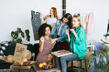 four young woman female caucasian and african students at swap party try on clothes, bags, shoes...
