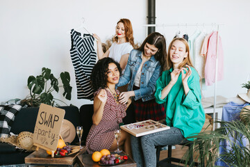 four young woman female caucasian and african students at swap party try on clothes, bags, shoes...