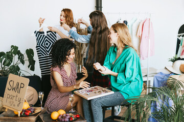 four young woman female caucasian and african students at swap party try on clothes, bags, shoes...