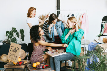 four young woman female caucasian and african students at swap party try on clothes, bags, shoes...