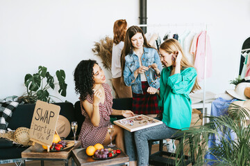 four young woman female caucasian and african students at swap party try on clothes, bags, shoes...